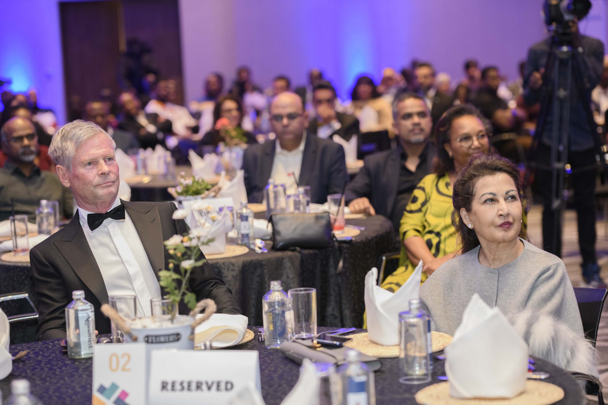 Guests in formal dress seated at a Safal Eye in the Wild gala dinner in a ballroom lit in blue.